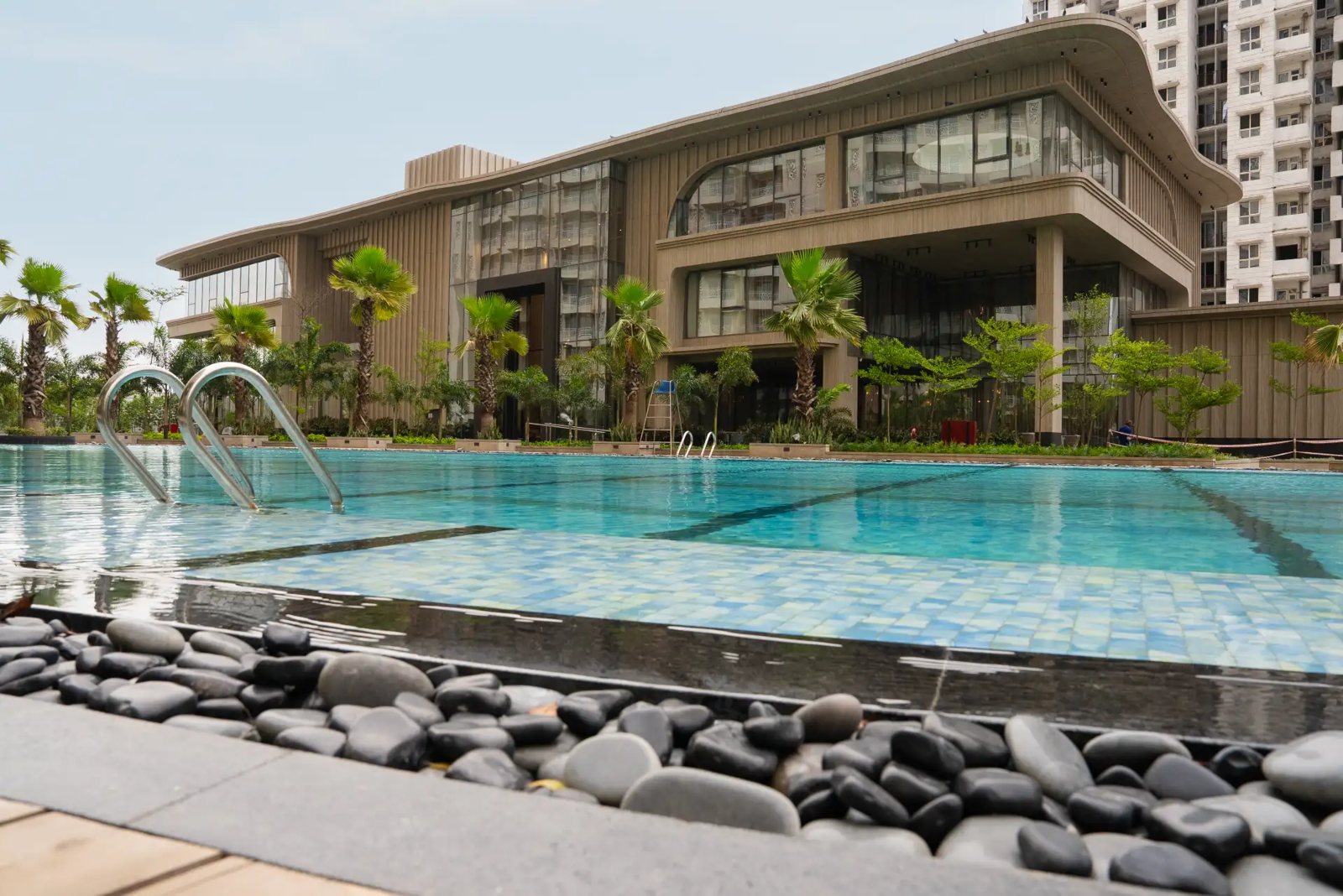 Club Mocha clubhouse in the built Phase 1 of the colony, a curved-roof building behind a large outdoor pool, with a Phase 1 tower to the right.